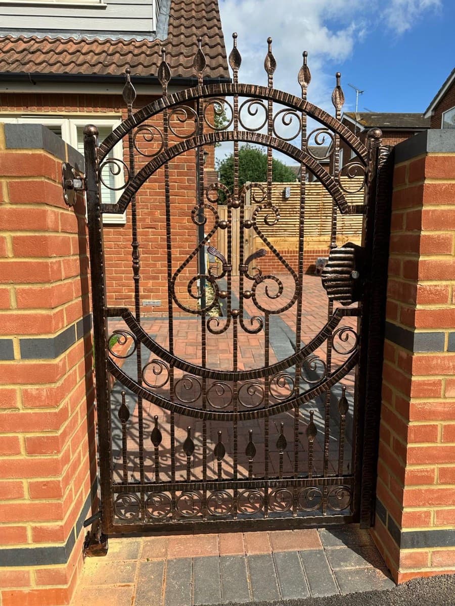 Ornate pedestrian steel gate set in brick pillars