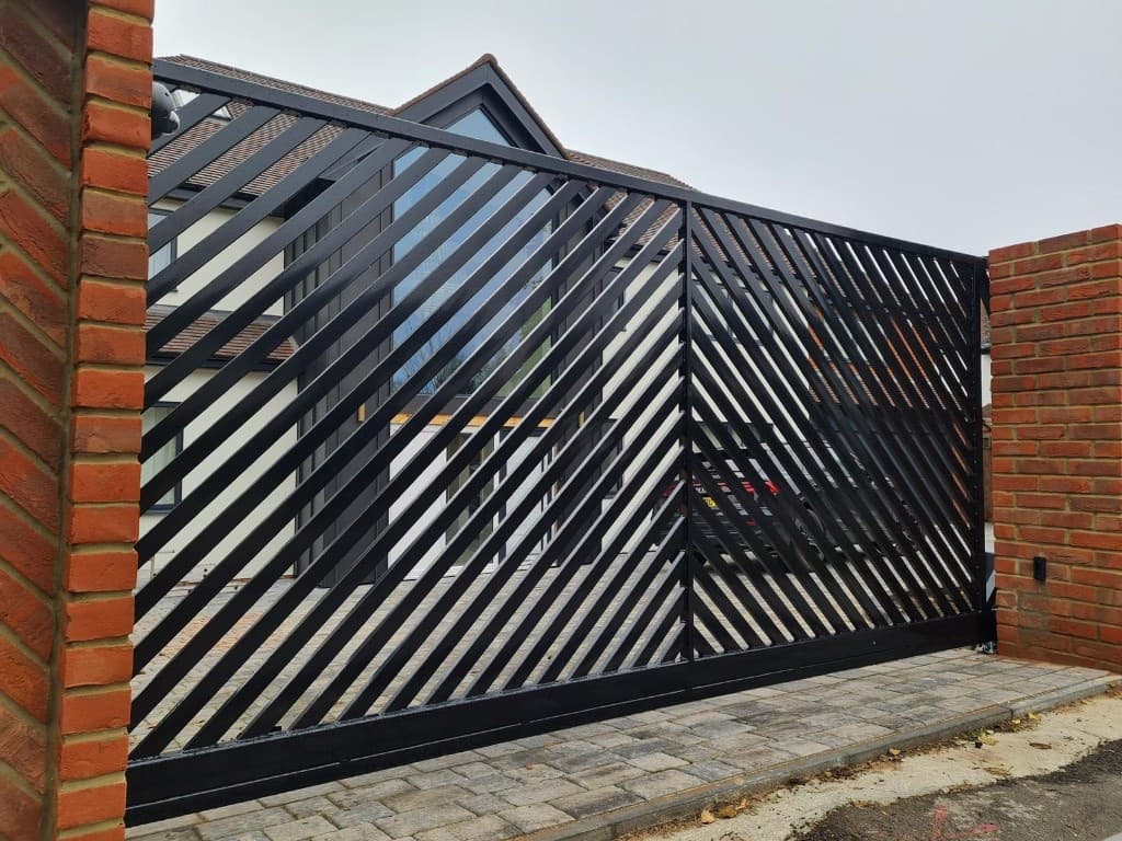 Modern black steel driveway gate with diagonal slat infill between brick pillars